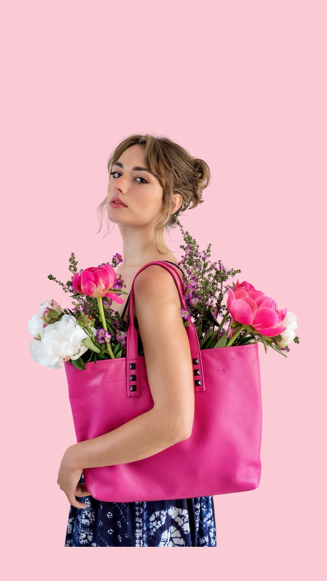 Woman holding a pink tote bag filled with flowers against a pink background